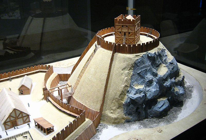 Model of a typical Motte and Bailey Castle, showing the artificial mound surmounted by a wooden keep, (the Motte), and the fenced enclosure surrounded by a ditch (the Bailey).
